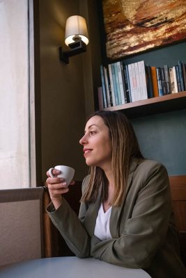 Photo of an enterprising young woman drinking coffee in a coffee shop smiling and looking out the window.
